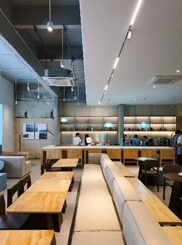 Modern café interior with warm wooden tables, cushioned seating, and an open bar area