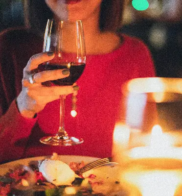 A woman holding a glass of red wine at a romantic dining table