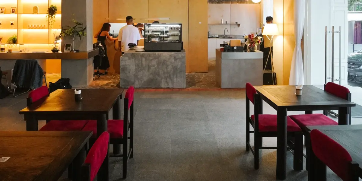 Warm minimalist café interior with wooden accents, red chairs, and an open coffee bar.