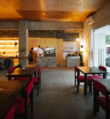 Warm minimalist café interior with wooden accents, red chairs, and an open coffee bar.