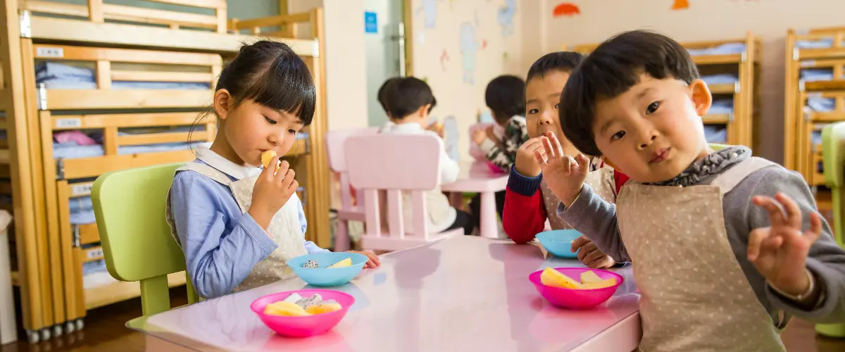 Children enjoying snack time together in a colorful preschool classroom.