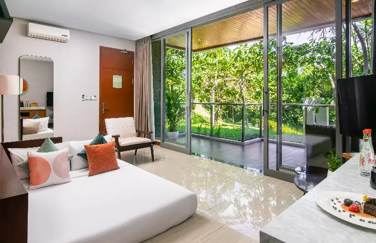 Modern villa room with workspace, large glass doors, and private balcony overlooking lush greenery.