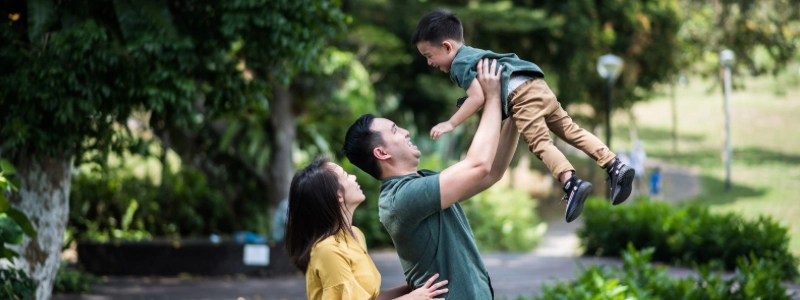 A_father_lifts_his_child_as_the_mother_watches_with_joy